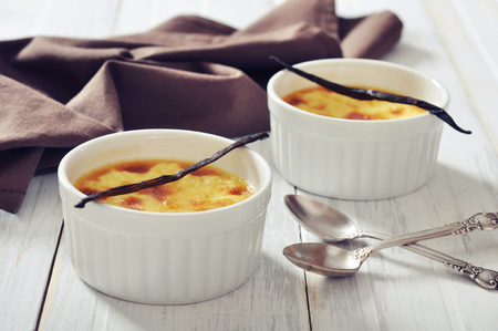 The creme brulee in ceramic baking mold with vanilla pod on wooden tableの写真素材