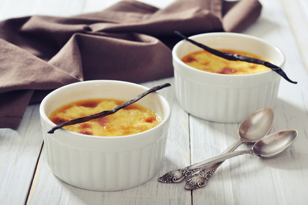 The creme brulee in ceramic baking mold with vanilla pod on wooden tableの写真素材