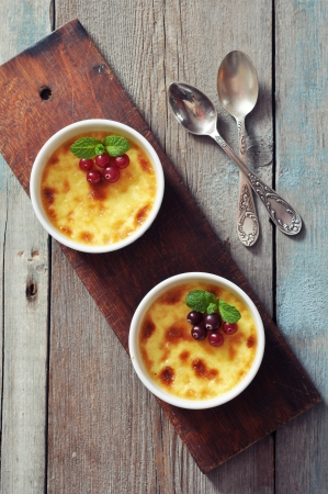 The creme brulee in ceramic baking mold with mint and berries on wooden tableの写真素材