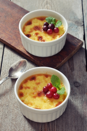 The creme brulee in ceramic baking mold with mint and berries on wooden tableの写真素材