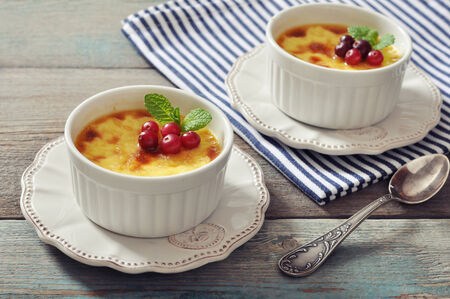 The creme brulee in ceramic baking mold with mint and berries on wooden tableの写真素材