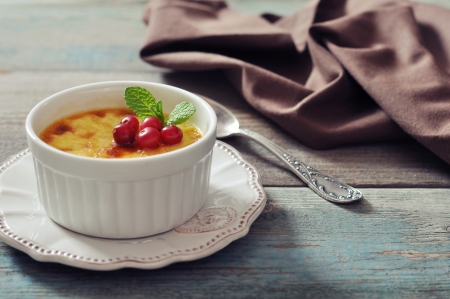 The creme brulee in ceramic baking mold with mint and berries on wooden tableの写真素材