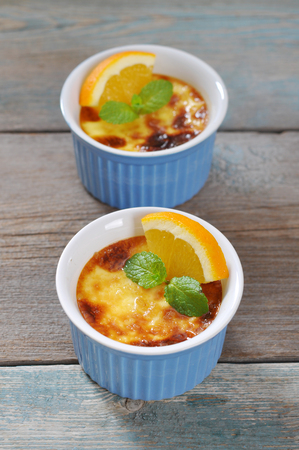 The creme brulee in ceramic baking mold with orange on wooden tableの写真素材