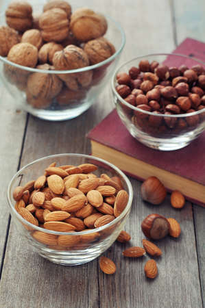 Almonds, walnuts and hazelnuts in glass bowls on wooden の写真素材