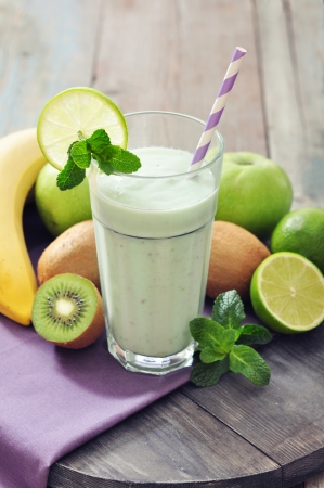 Banana smoothie with kiwi, apple, lime and mint on wooden backgroundの写真素材