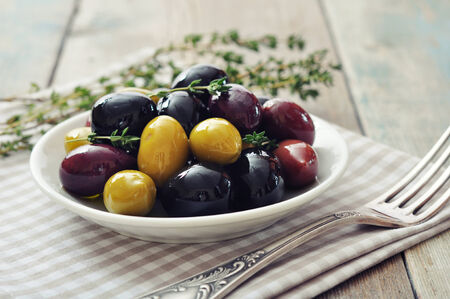 Different kinds of olives on plate with fork on wooden backgroundの写真素材