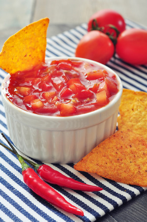 Bowl of salsa with tortilla chips, tomatos and chilli pepper closeup  on white dishの写真素材