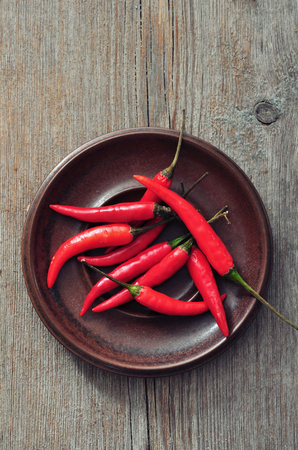 Red chili pepper on brown plate on old wooden tableの写真素材