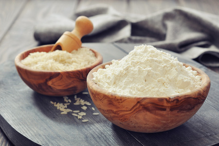Raw rice and flour in bowls with scoop on wooden backgroundの写真素材