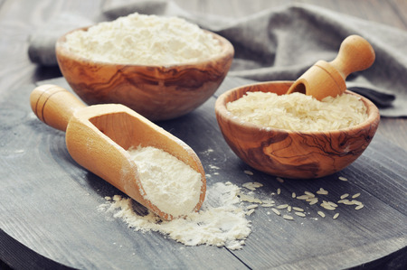 Raw rice and flour in bowls with scoop on wooden backgroundの写真素材