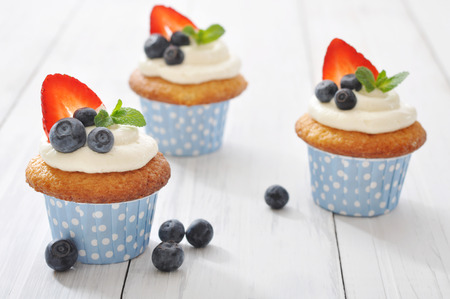 Cupcakes decorated with butter cream and fresh berries in polka dot cases on wooden backgroundの写真素材
