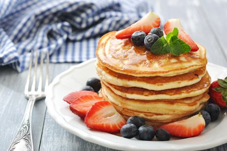 Pancakes with fresh berries, mint and maple syrup on white plate closeupの写真素材