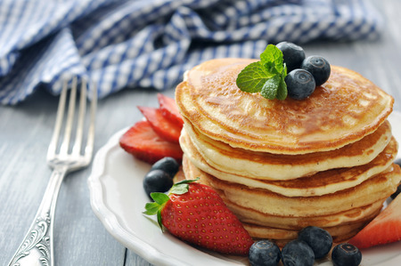 Pancakes with fresh berries, mint and maple syrup on white plate closeupの写真素材