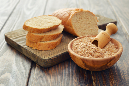Wheat bran in bowl with sliced bread on wooden backgroundの写真素材