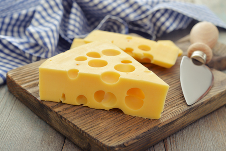 Cheese with big holes and knife on wooden cutting boardの写真素材