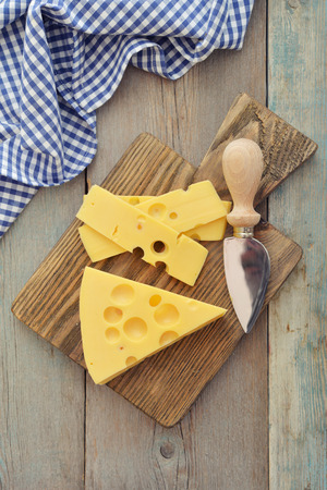 Cheese with big holes and knife on wooden cutting boardの写真素材