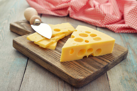 Cheese with big holes and knife on wooden cutting boardの写真素材