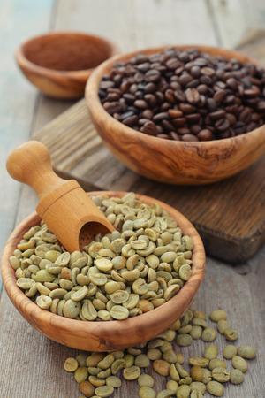 Green and roasted coffee beans  in wooden bowl closeupの写真素材