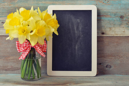 Small wooden framed blackboard with daffodils on wooden backgroundの写真素材