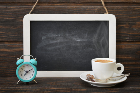 Cup of coffee with blackboard and alarm clock on wooden backgroundの写真素材