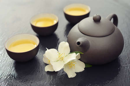 Green tea in cups with jasmine flowers and teapot on wet  graphite backgroundの写真素材