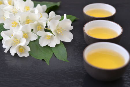 Green tea in cups with jasmine flowers on wet  graphite backgroundの写真素材