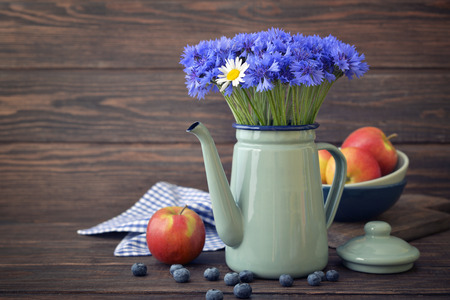Cornflowers with daisy in  kettle with apples on wooden background closeupの写真素材