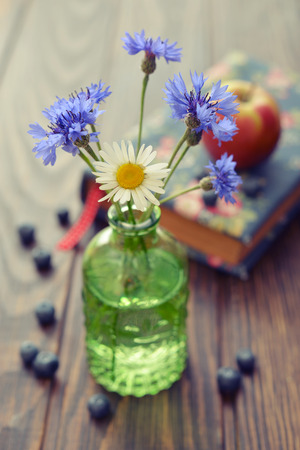 Cornflowers in vintage bottle with berries on wooden backgroundの写真素材