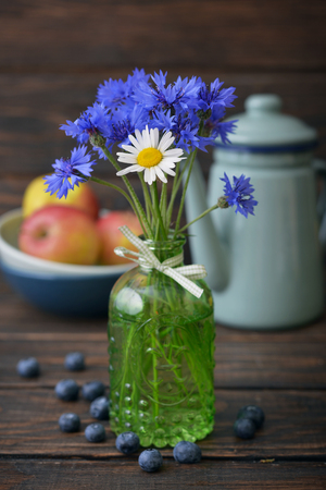 Cornflowers in vintage bottle with berries on wooden backgroundの写真素材