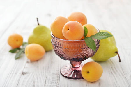 Fresh ripe apricots in glass ramekin and pear on wooden の写真素材