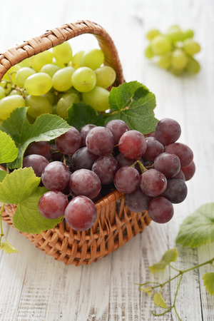 Red and green grapes in wicker basket on a wooden background の写真素材