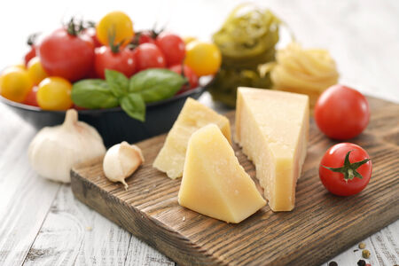 Parmesan cheese on cutting board with basil and tomato on wooden backgroundの写真素材