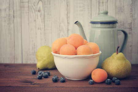 Apricots in bowl with fresh pear and blueberry on wooden backroundの写真素材