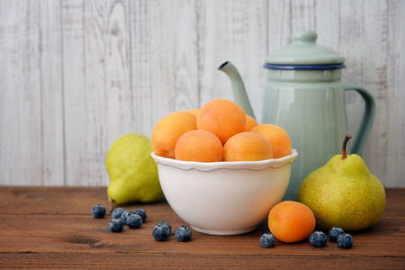 Apricots in bowl with fresh pear and blueberry on wooden backroundの写真素材