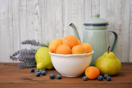 Apricots in bowl with fresh pear and blueberry on wooden backgroundの写真素材