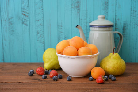 Apricots in bowl with fresh pear and blueberry on wooden backgroundの写真素材