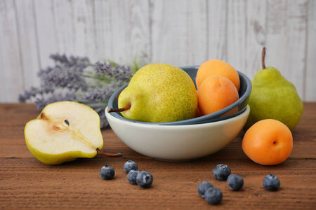 Pear in bowl with fresh blueberry, apricot and lavender flowers on wooden background
の写真素材