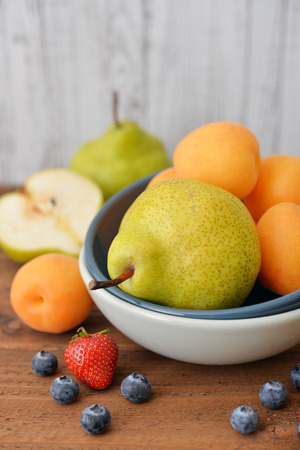 Pear in bowl with fresh blueberry and apricot on wooden backgroundの写真素材