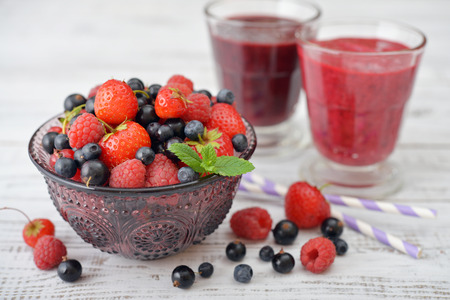 Fresh ripe berries in glass vase with smoothies on light backgroundの写真素材