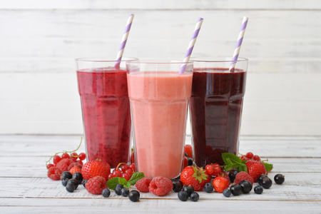 Three glasses of smoothies with different berries on wooden backgroundの写真素材