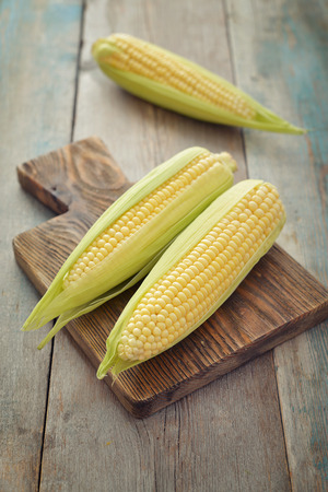 Raw corn cobs on wooden background closeupの写真素材