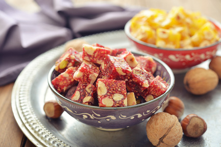 Turkish delight with nuts and sesame in ceramic bowl on wooden backgroundの写真素材