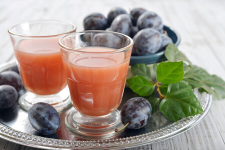 Plum juice in glass with fresh plums on wooden backgroundの写真素材