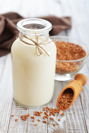 Buckwheat milk in bottle  with dry buckwheat seeds on white  wooden background. Vegan and vegetarian milk concept.の写真素材