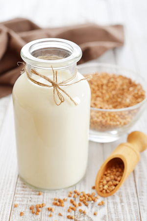 Buckwheat milk in bottle  with dry buckwheat seeds on white  wooden background. Vegan and vegetarian milk concept.の写真素材