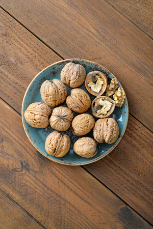 Walnut kernels and whole walnuts on plate on rustic old wooden backgroundの写真素材