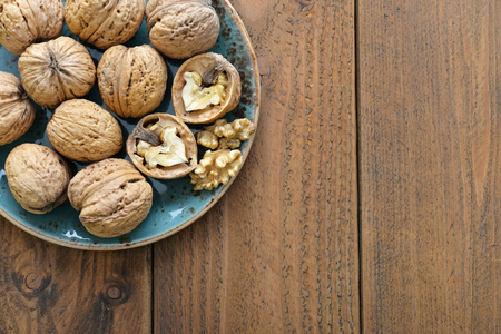 Walnut kernels and whole walnuts on plate on rustic old wooden backgroundの写真素材