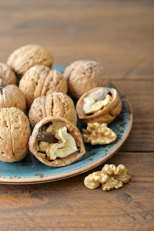 Walnut kernels and whole walnuts on plate on rustic old wooden backgroundの写真素材