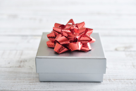 Silver gift box with red ribbon over white wooden backgroundの写真素材