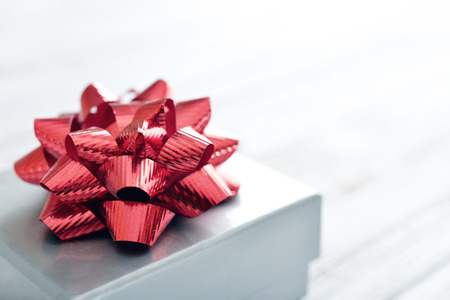 Silver gift box with red ribbon over white wooden backgroundの写真素材